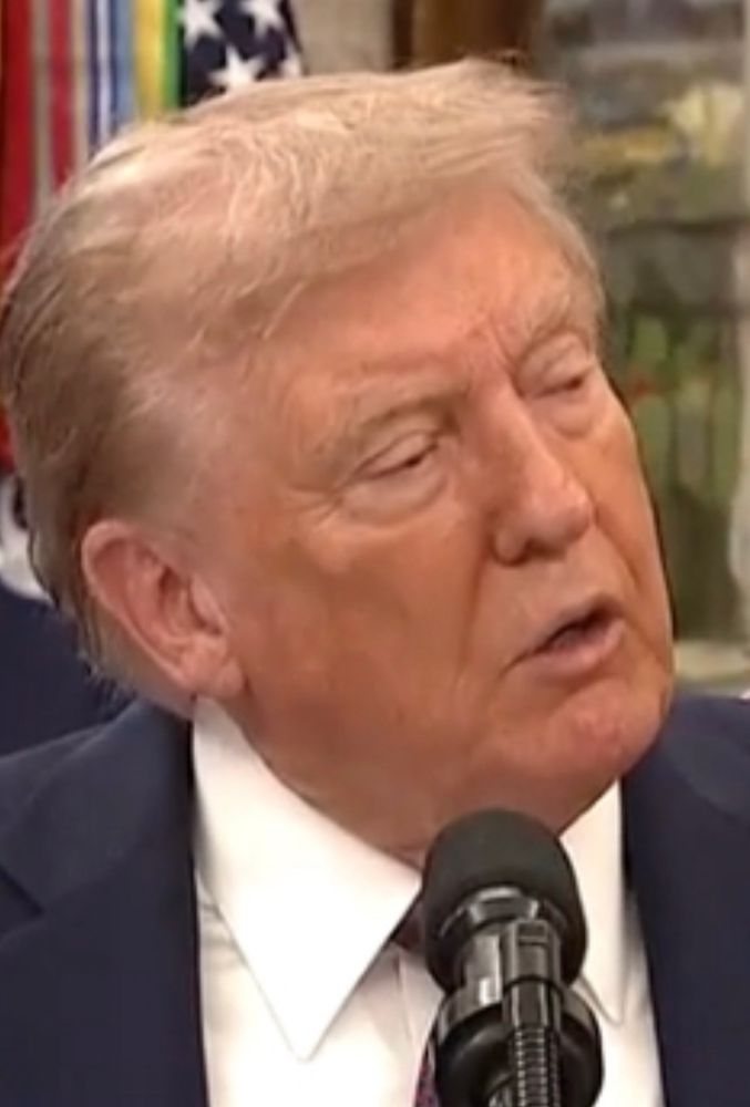 An ill orange man stands behind a microphone. He has puffy eyes and prominent swelling on his cheekbones