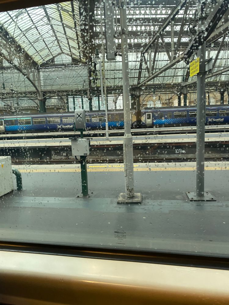 Glasgow central station on a rainy day from the perspective of someone sitting on a train looking out to the platform 