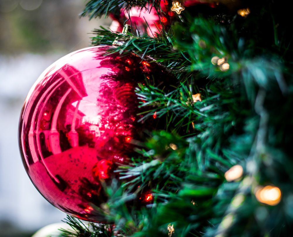 A close-up of red Christmas ornament on a green outdoor tree reflecting the Walterboro, SC, city hall. 