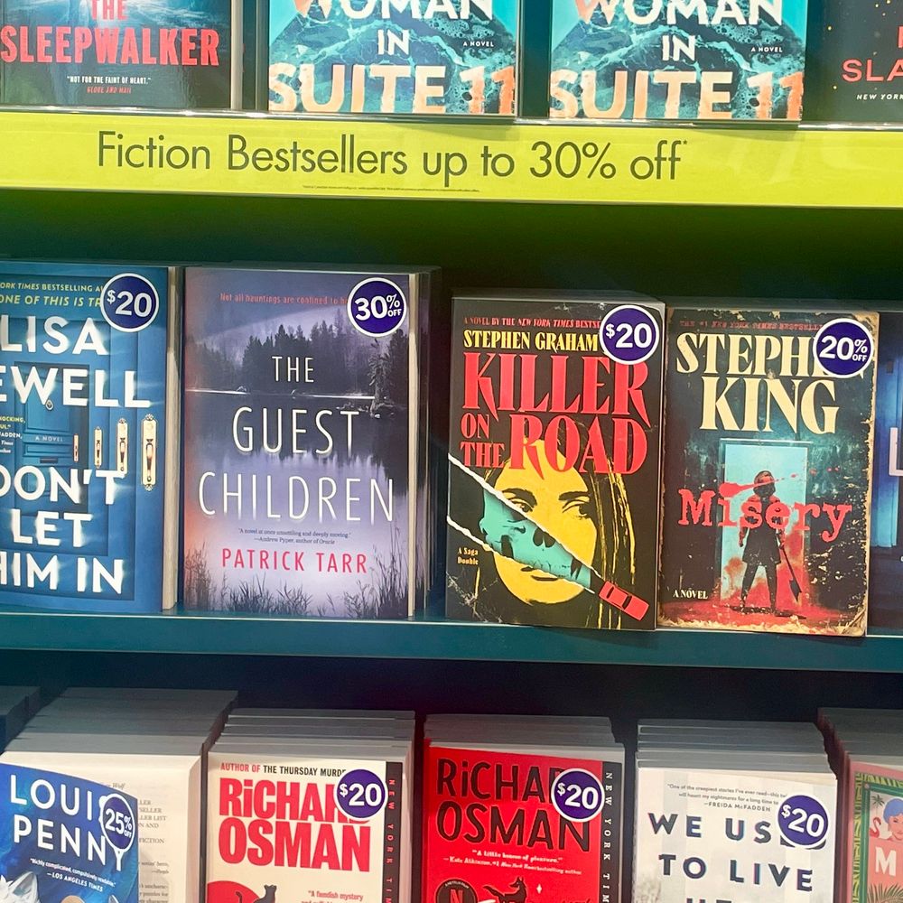 A photo of the book #TheGuestChildren on a store shelf next to Stephen Graham Jones’ Killer on the Road and Stephen King’s Misery. 