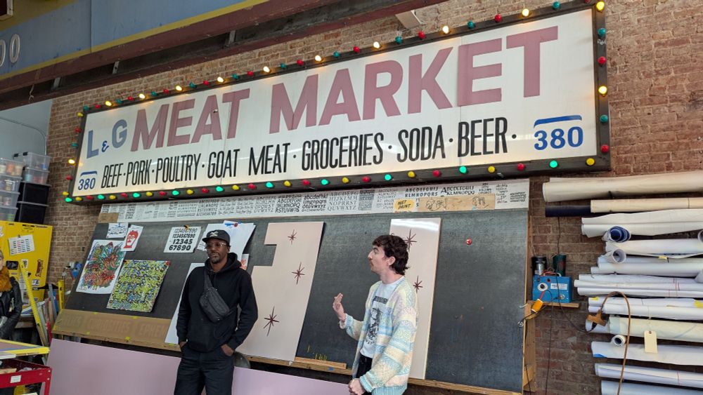 two men standing in front of an old sign that says "L&G Meat Market"
