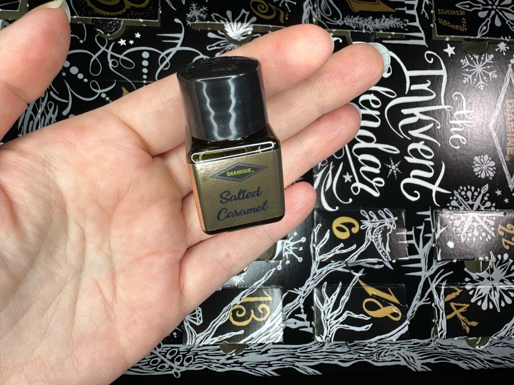 Front of the same sample bottle of Diamine ink from the 2024 Black Edition Inkvent. The ink is Salted Caramel.
