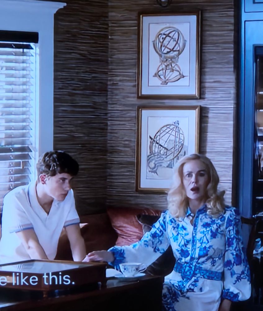 Nicole Kidman in a blue and white dress and a young male actor in a white polo shirt sit on a corner sofa; there is a cup and saucer on the table in front of them, and they are holding hands. (Kidman is playing the younger actor's mother in this drama). On the wall behind are two mounted and framed reproductions of prints from a coloured copy of Tycho Brahe's Astronomiae Instauratae Mechanica (1598).