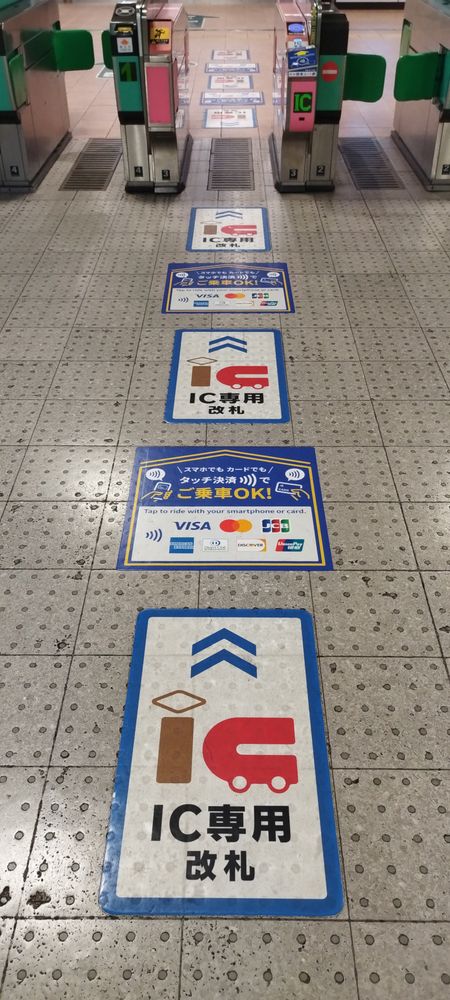 真ん中の自動改札機はカード専用改札（磁気券対応不可）で、ここのみがクレカのタッチ決済対応。
その改札に向かってIC専用改札とクレカタッチ決済対応のフロアステッカーが床に並べ貼られ、誘導する。改札機の先の反対側も同様。

もっともICカードはそれ以外の改札機も利用可能なのだが。
（2025/8/8　西鉄久留米駅・中央改札口）