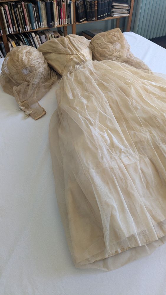 An 1830s wedding gown in need of restoration made of silk and tulle, leg of mutton sleeves.