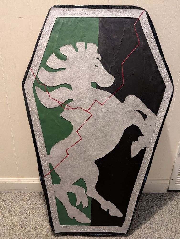 A larp shield- black and green fake wood texture with steel framing in the shape of a zebra rampant. Red cracks spider through it. 
