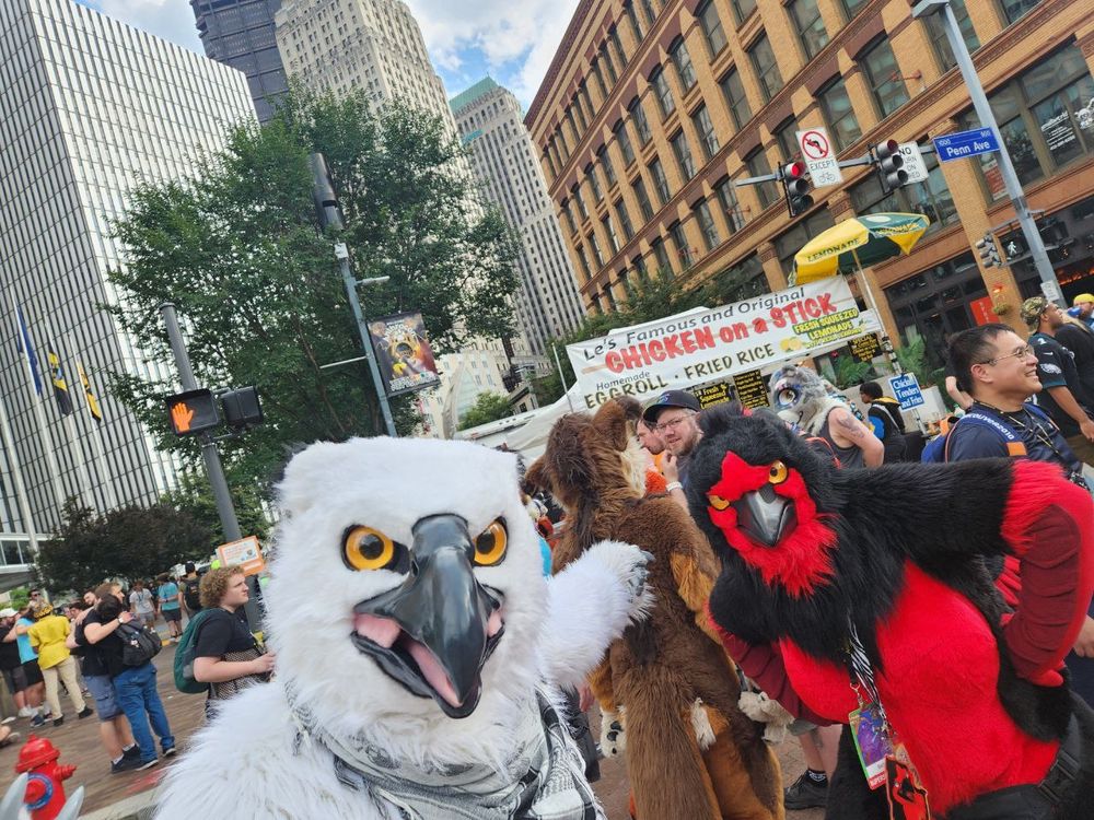 two bird fursuiters looking disgruntled in front of a 'chicken on a stick' sign