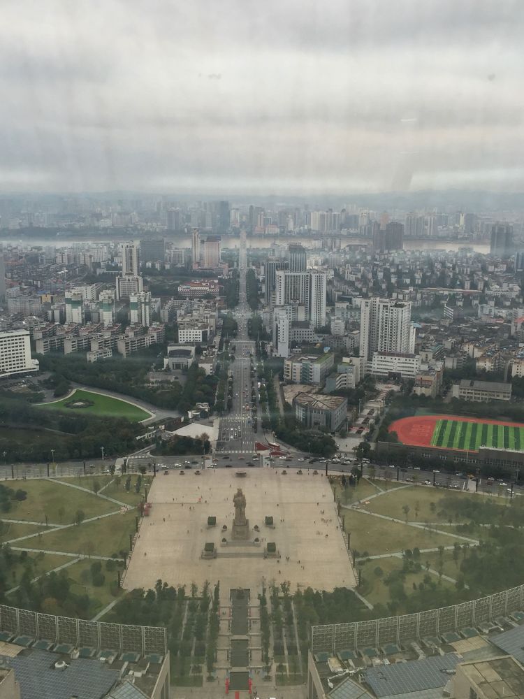 A view of Zhuzhou from above showing a park with a square and a statue in the centre followed by a boulevard leading through the city to a river in the background. 
