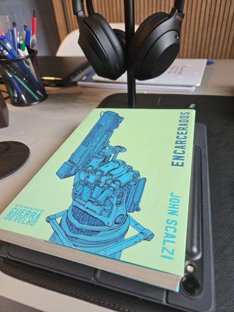 Livro "Encarcerados", de John Scalzi, em cima de um tablet que está em cima de uma mesa.