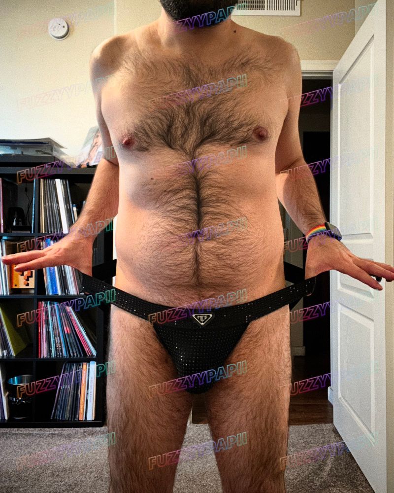 Hairy guy wearing only an MCE black rhinestone covered jockstrap. He’s holding the edge/bands out. 