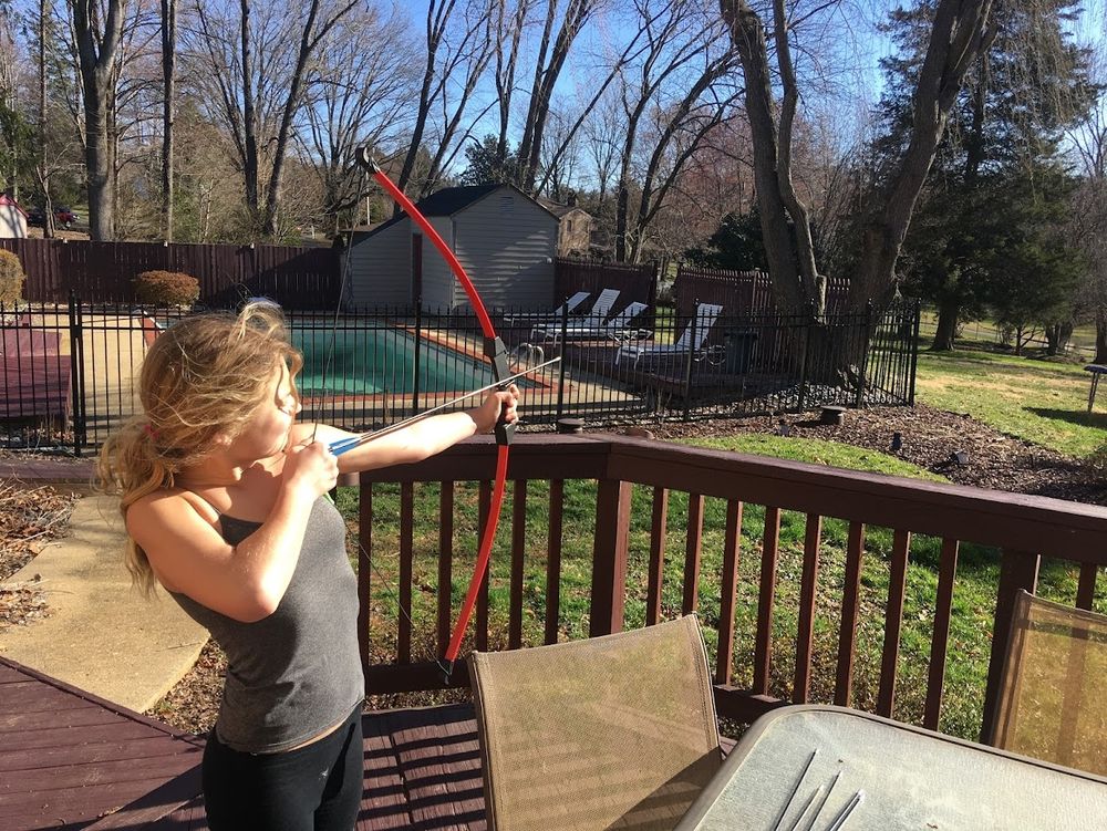 Our Gen Z Daughter shooting a silver arrow off our back deck into the yard from a red and black bow