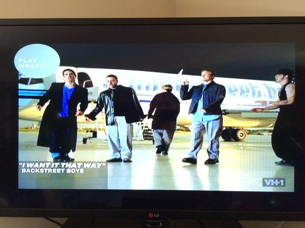 A TV showing VH1 playing the Backstreet Boys music video for “I Want It That Way” showing the members of the band in front of a white private jet in a hangar