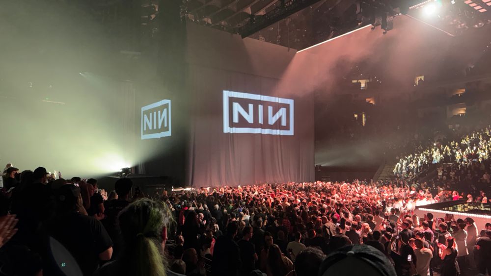 A picture of a crowded arena with a box covered in cloth with the letters NIN projected on it