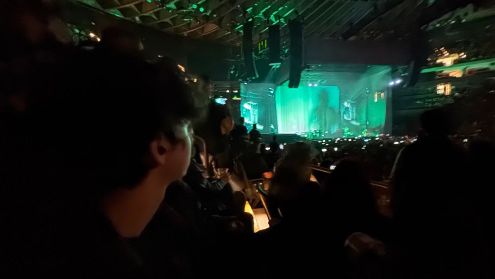 A picture of a crowd looking at a green lit stage at a rock concert
