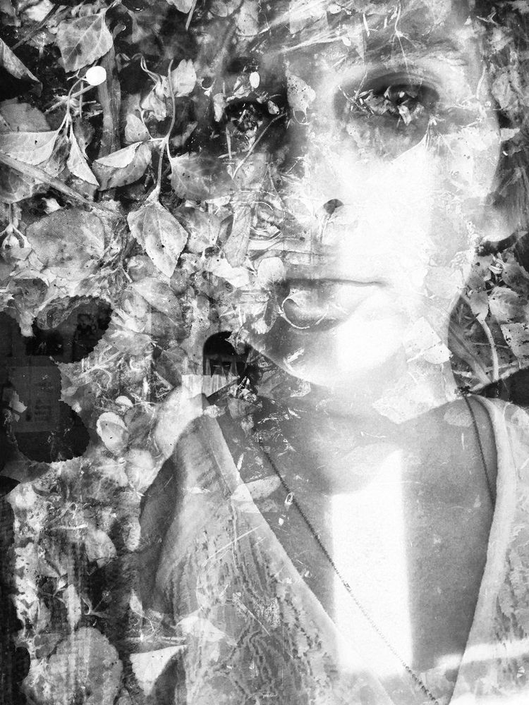 Black and white photographic double exposure of Mickey’s face and neckline with a large white rectangle of light running vertically down their face to their chest. Photo is blended with one of leaves and bits on the ground, making areas around the light become obscured and jumbled. 