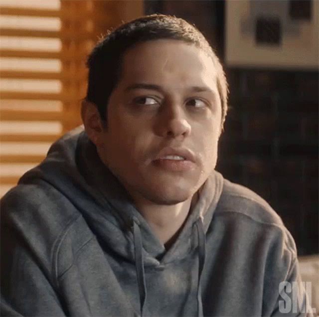 a man in a gray hoodie is looking at the camera with a serious look on his face .