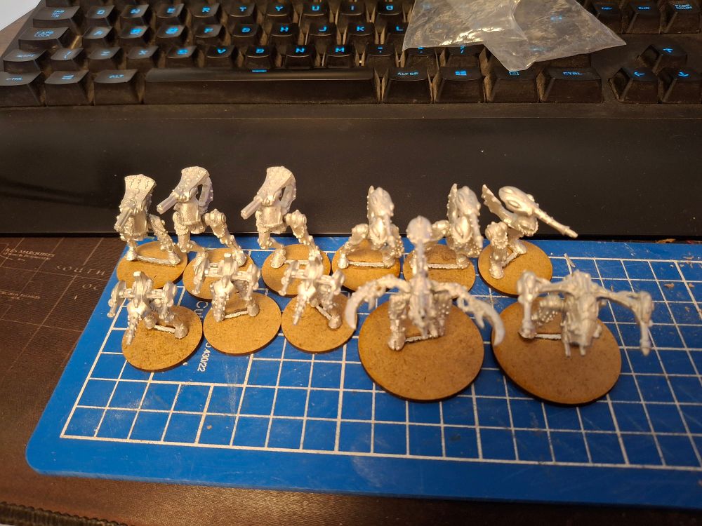Cute little Epic 40,000 Slaanesh walkers. Shiny metal models on round mdf bases. Freshly put together on a blue cutting mat. The models waiting and hoping to be painted... ha!