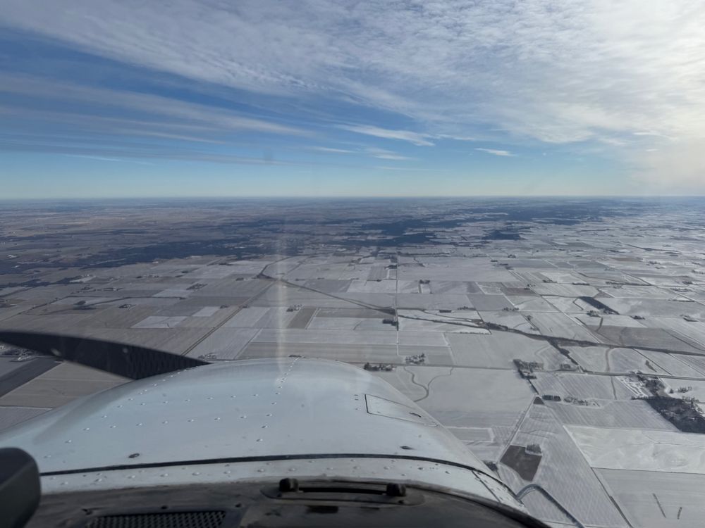 View out the windshield from the cockpit of a general aviation aircraft looking out a snow covered ground and blue skies with cirrus clouds 