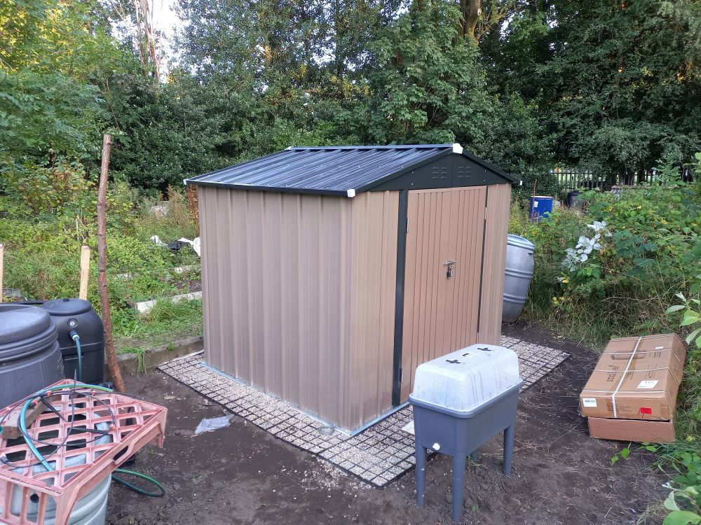 A metal shed with black roof and brown walls and doors.