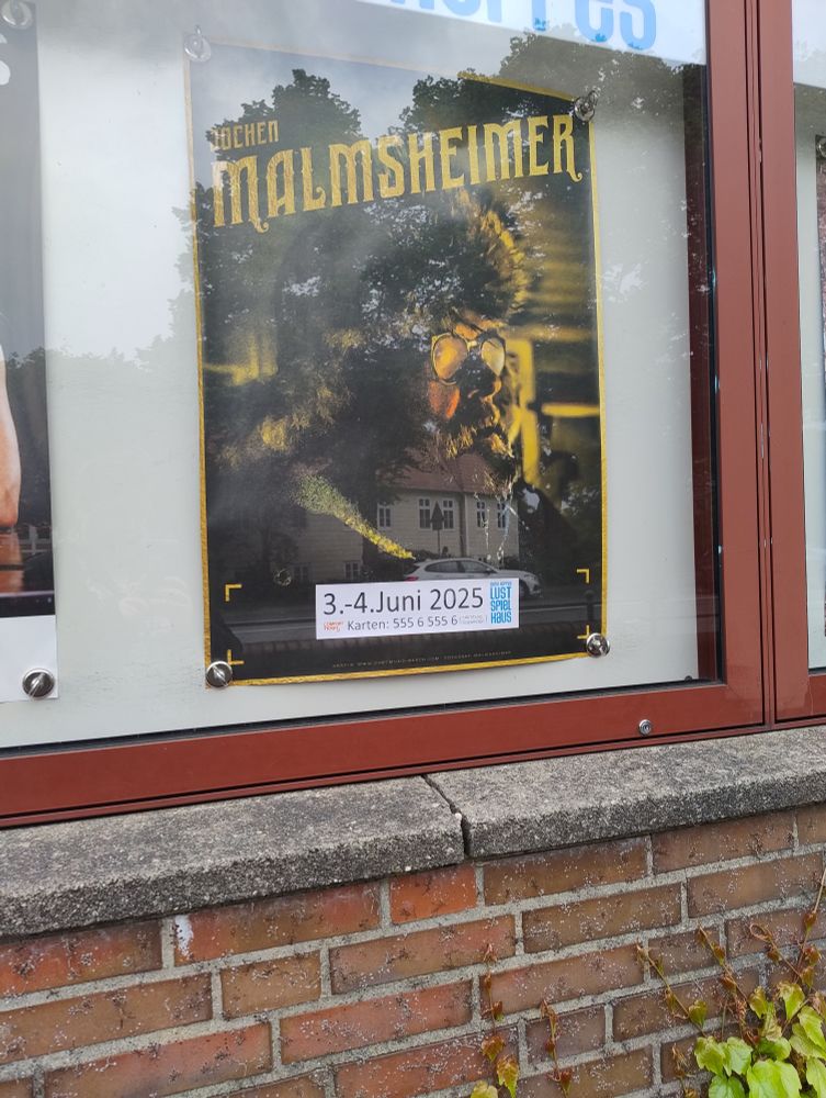 Plakat an der Programmwand des Alma Hoppe Lustspielhauses. In großen Lettern steht oben "Jochen Malmsheimer". Darunter ein Foto von eben jenem in einem winterlich wirkenden Parka mit Fellbesatz an der Kapuze.