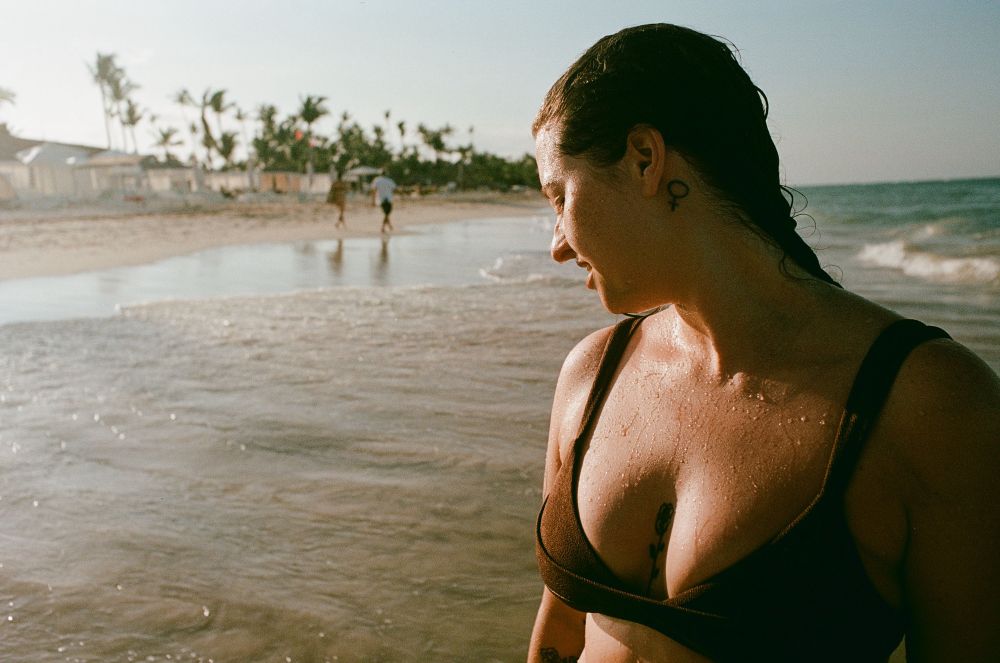 Foto da minha esposa após um banho de mar no final da tarde. Ela está olhando para o lado e é possível ver a água escorrendo em seu peito