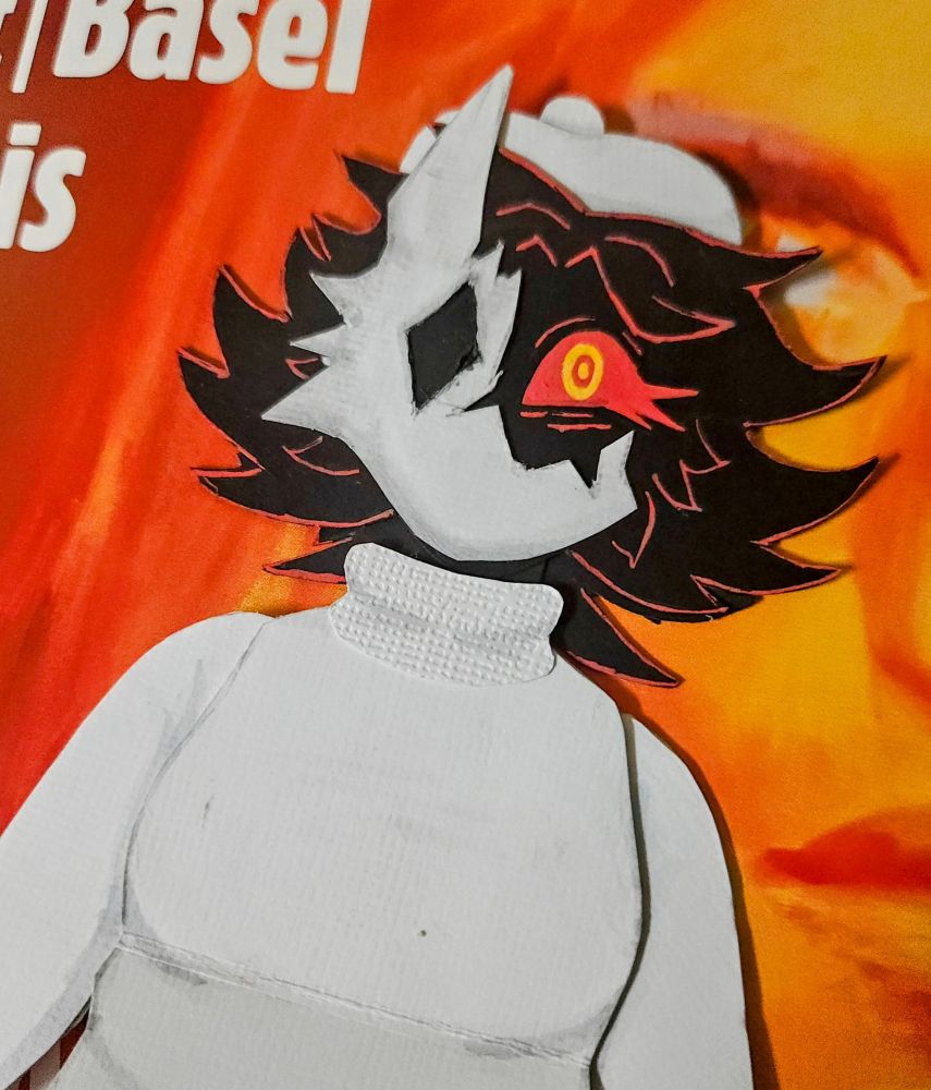 A closeup of the top half of a detailed paper doll of Folly, an antagonist from the game Regretevator. She is a humanoid character who is solid black in color, with medium length, spiky hair, clawed fingers with red tips, and a single visible eye that is bright red with sharp lower lashes. The iris and pupil of her eye are made up of two bright yellow concentric rings.

From what is visible in this image, wears a white turtleneck sweater, and a white beret on her head. On her face she wears a broken mask that resembles some sort of animal. The mask has a single, diamond shaped hole for an eye, three spikes on the outer edge that look like fur, and a single, tall ear pointing upwards. The missing piece of the mask reveals her eye.

The closeup shows details of her hair and face, as well as some of the textures and shading used

The doll is displayed against a red, orange, and yellow background that is a poster for a Paris art show.