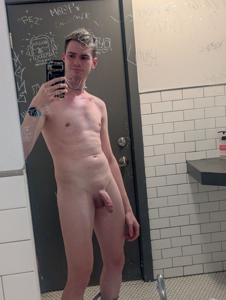 nude of me from the front in a bathroom mirror. i am wearing a spiky choker and there are etched graffiti around my face on the mirror. 