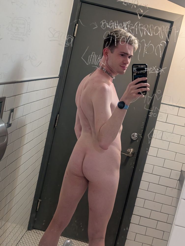 nude of me from the back in a bathroom mirror. i am wearing a spiky choker and there are etched graffiti around my face on the mirror. 