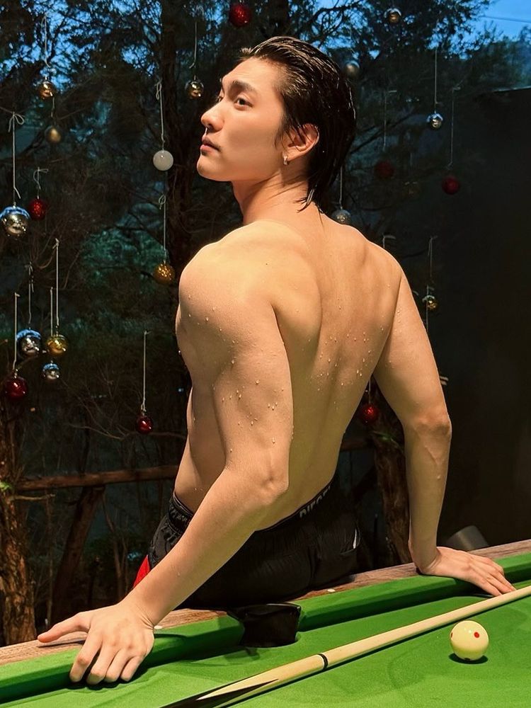 Boss Chaikamon shirtless and with his wet hair slicked back. His face is in profile and he is leaning back on a pool table with the picture taken from behind. There are water droplets still clinging to his skin. 