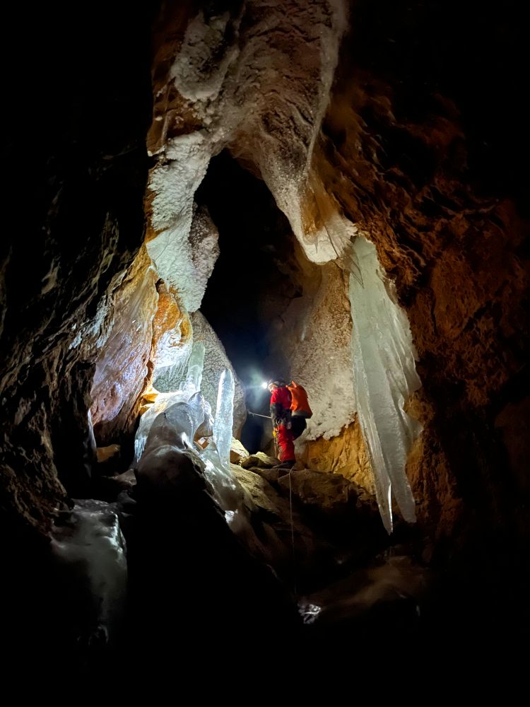 Inside a cave, a caver uses ropes to climb a steep rock face between ice waterfalls. 