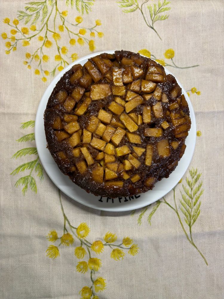 Vista cenital de Bizcocho con manzana caramelizada porcima. Está sobre un plato blanco que dice en el borde “im fine” que a su vez reposa sobre un trapo con dibujos de flores de mimosa 