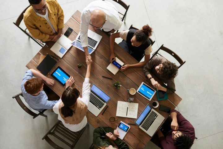 People sat at a table with two people shaking hands across the table, stock image from Pexels. 