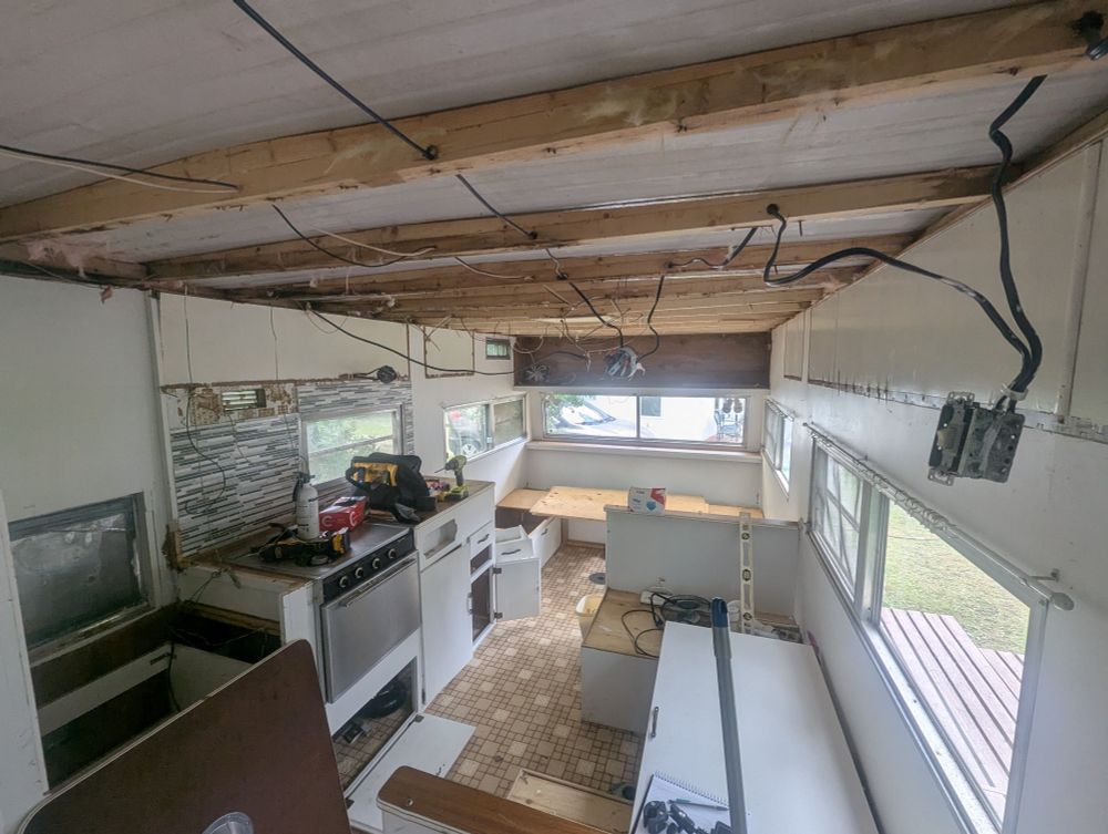 Interior of a travel trailer with cabinets & ceiling torn out and wires hanging. 