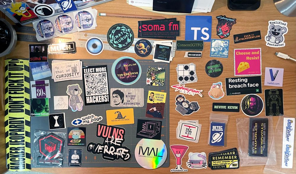 aerial view of stickers laid out on a desk from recent hacker cons in 2023