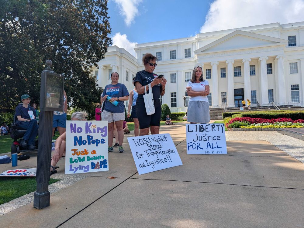 Protestors holding signs saying “No King No Pope Just A Low Down Lying Doprs;” “Rosa wouldn’t stand for Trump’s corruption and i justice” and “Liberty and Justice for All”