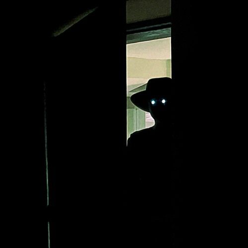 Man in hat with glowing eyes opening door from lighted hallway
