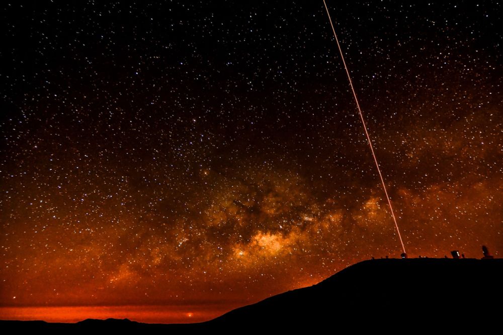 Laser beam sent upwards against a dark background, with tones of red and orange.