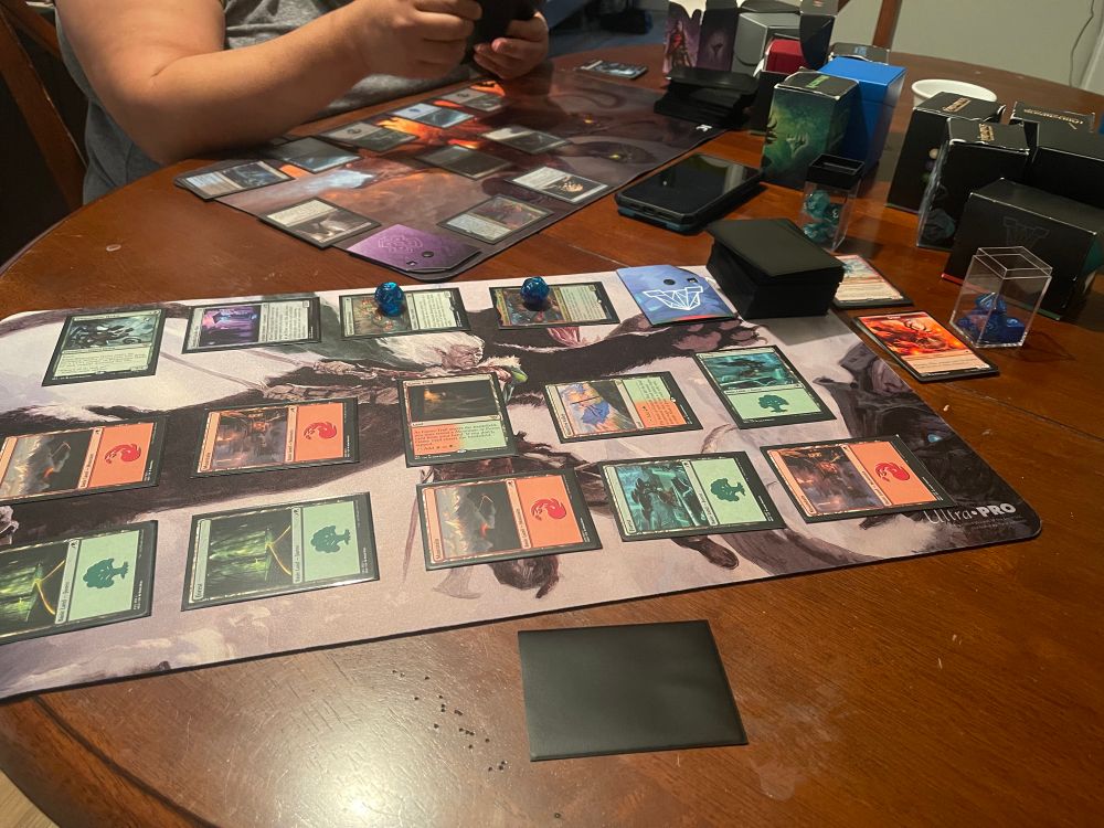 Two players playing Magic the Gathering. One is playing “Anowon, the Ruin Thief” and the other “Chishiro, the Shattered Blade” Commander Decks. 
