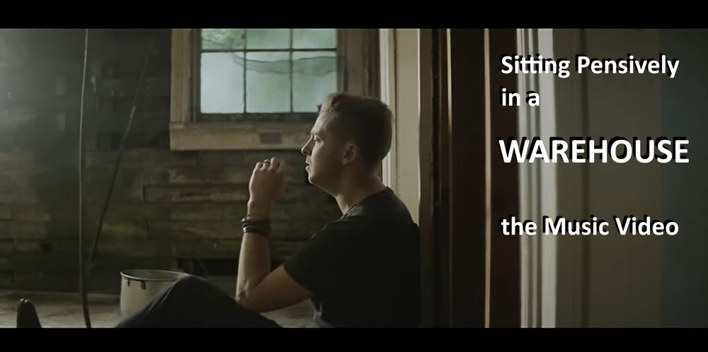 A still from the music video for the song Counting Stars, with my added caption "Sitting Pensively in a WAREHOUSE the Music Video," just my way of havin' some fun at the idea of "hey let's film our music video in a warehouse" being so generic.