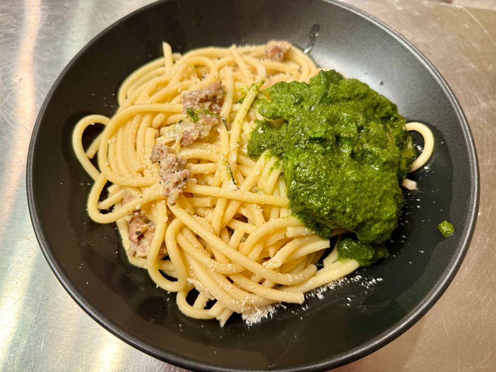 A black bowl of pasta and green chicken