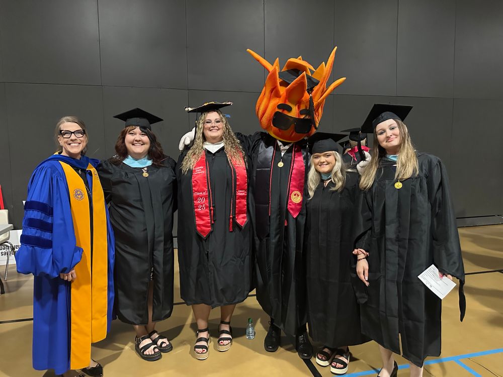 Graduating students and professor with university mascot who looks like a little fire