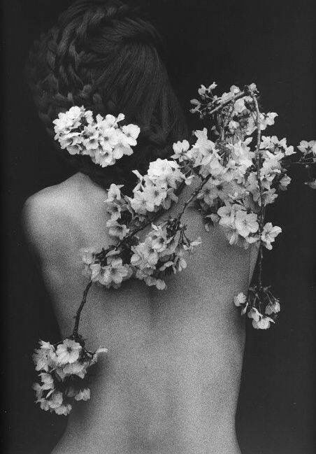 Lady with her back bared and blooms hanging from her hair and down her limbs 