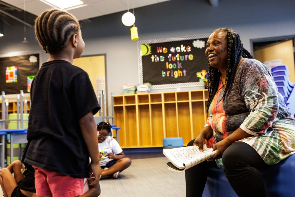 A woman enthusiastically smiles at and listens to a small child who faces her. 