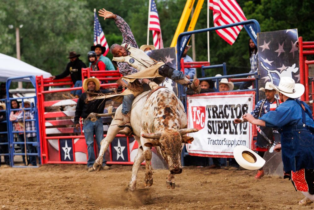 An audience watches as a man holds onto a saddle with one arm and has the other waving in the air as the bull he is riding attempts to throw him off. 