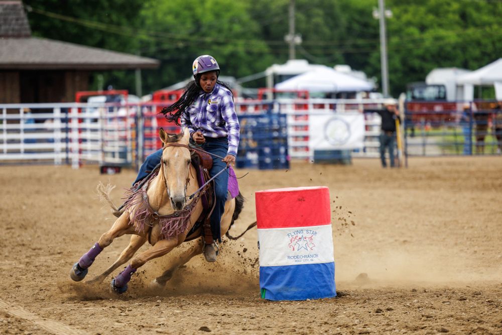 A young woman dramatically rides a horse around a multicolor barrel.