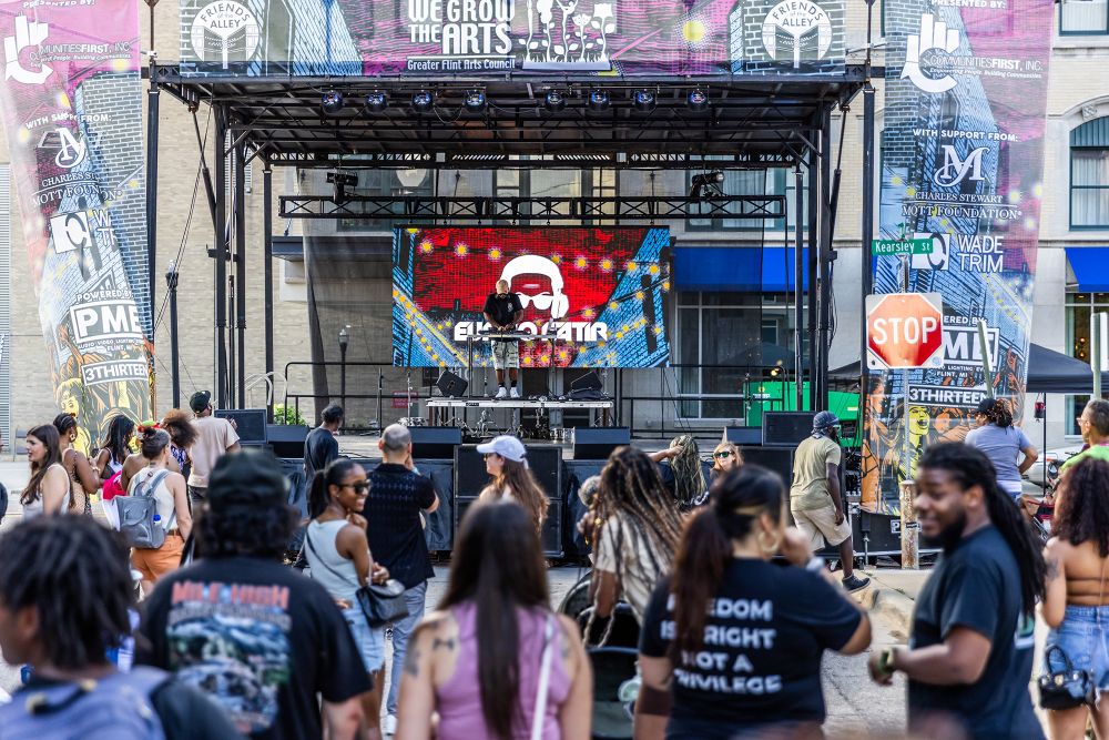 A group gathers in front of a performer on an outdoor stage. 