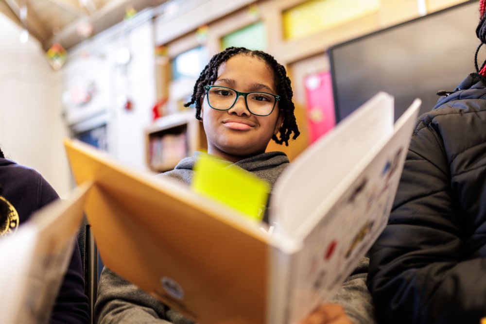 A child looks at the camera over an open book.