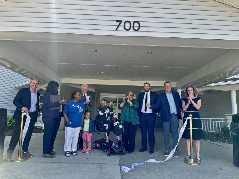 A group of people cheer as a ribbon is cut in front of a building.