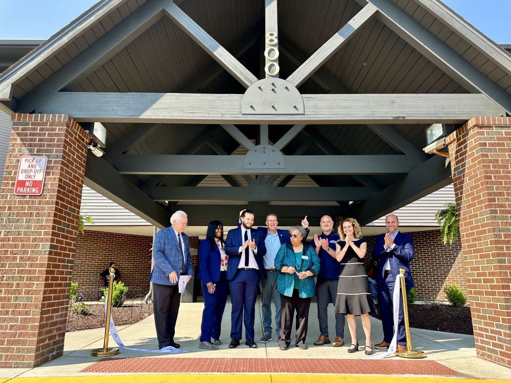 A group of people cheer as a ribbon is cut in front of a building.