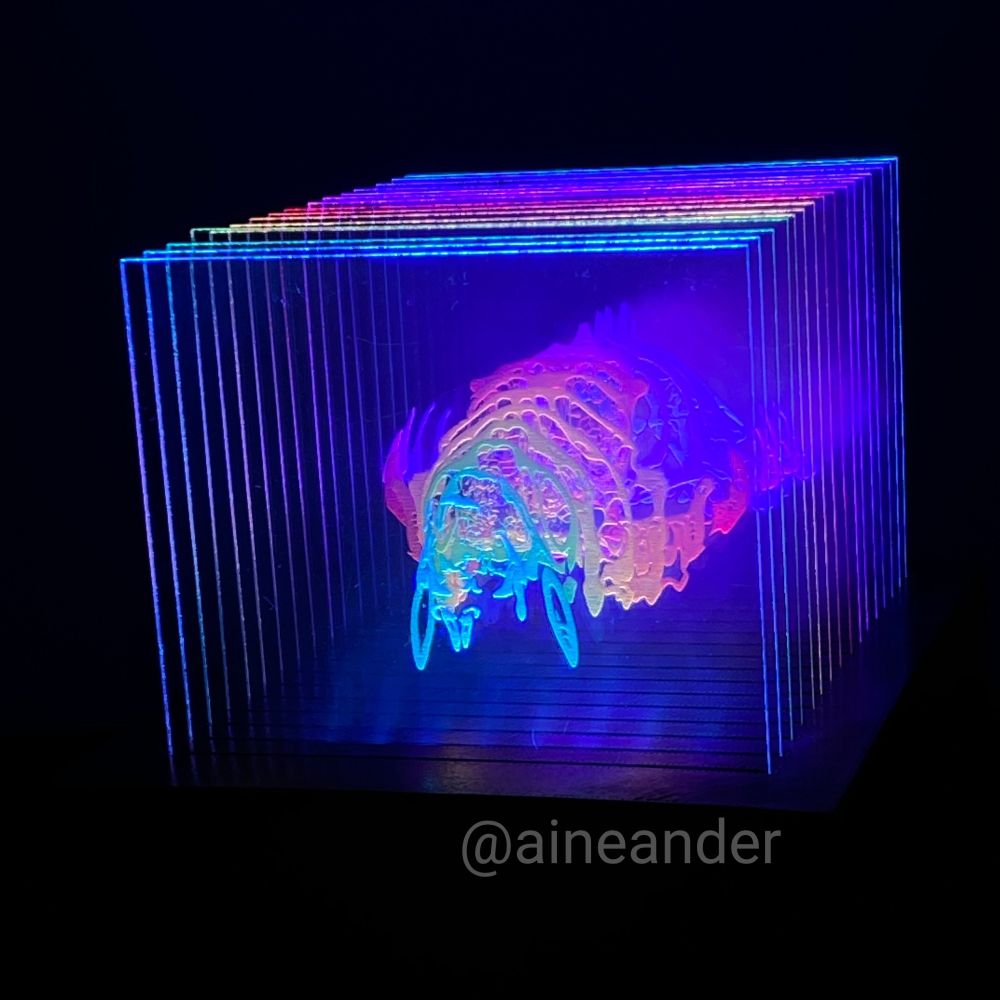 Photograph - A lit structure in a dark room stands out. It has many slices lit up in rainbow colors that creates the form of an opossum skull. 
